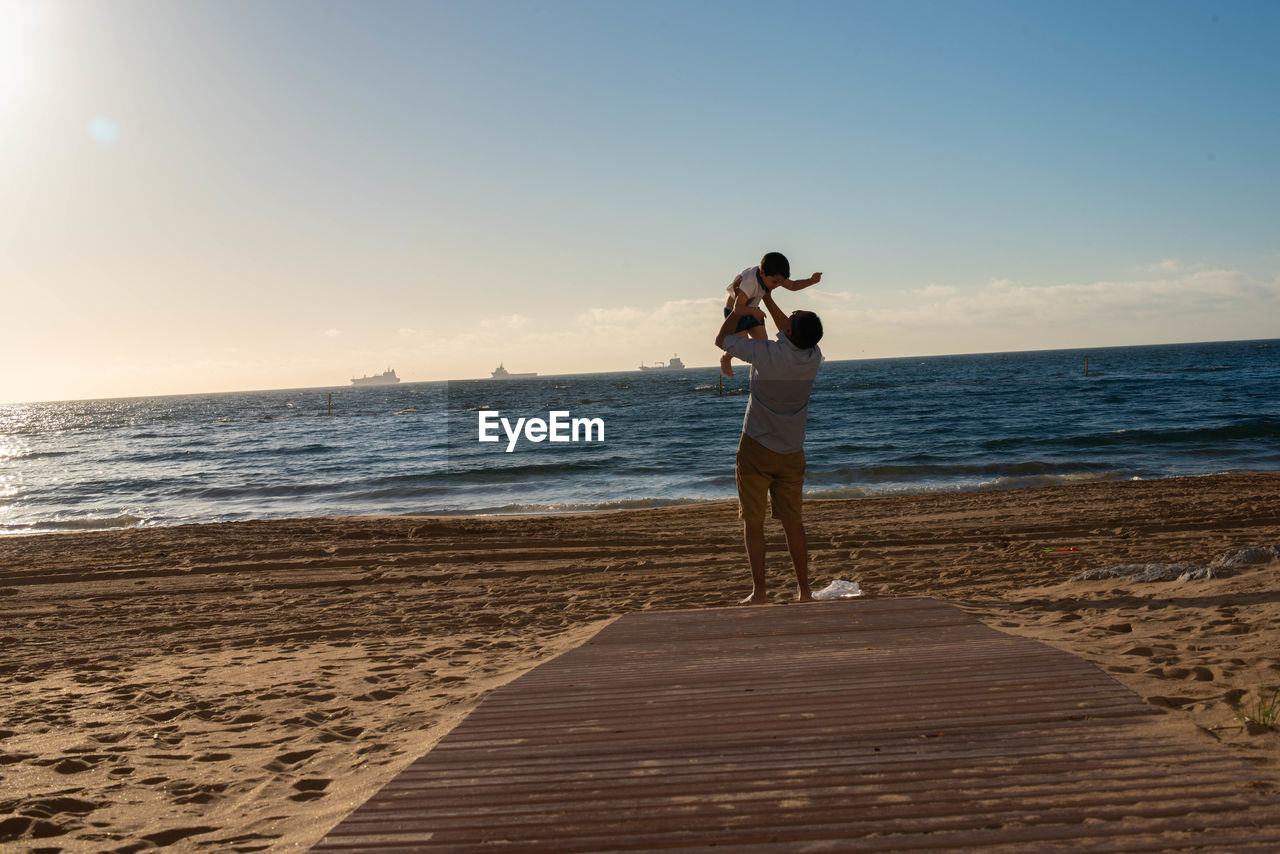 Happy father with son at beach against sky