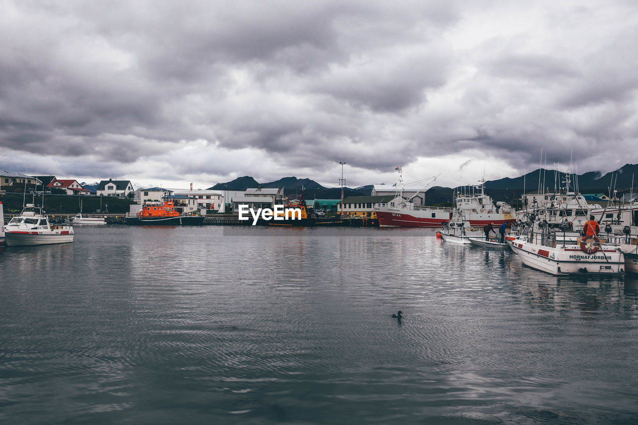 Boats moored at harbor against cloudy sky