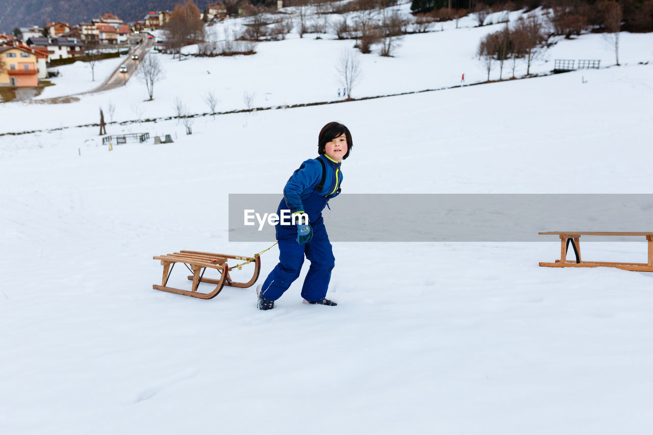 Smiling girl with short dark hair pulling up the wooden sled in snowy mountain