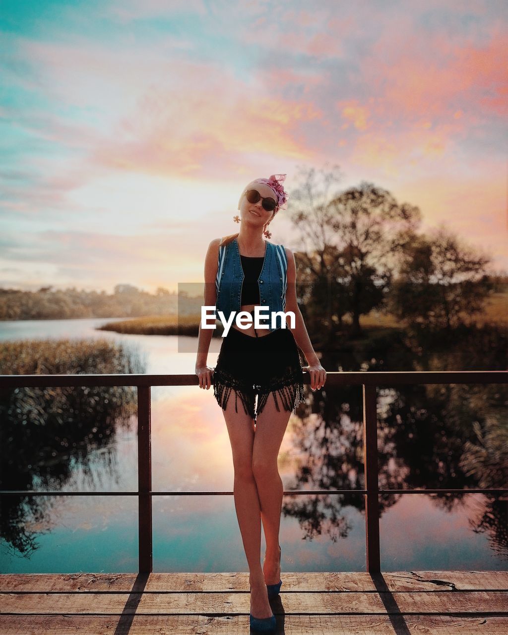 Full length of young woman standing on pier over lake against sky