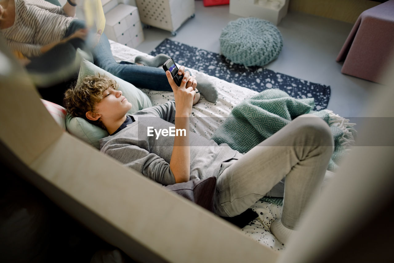 Boy lying on bed wile using smart phone