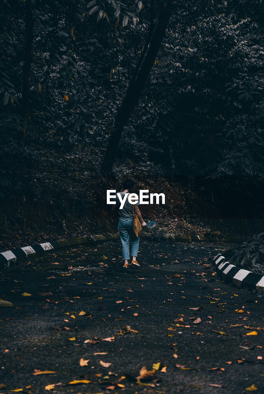 Rear view of woman walking on road in forest