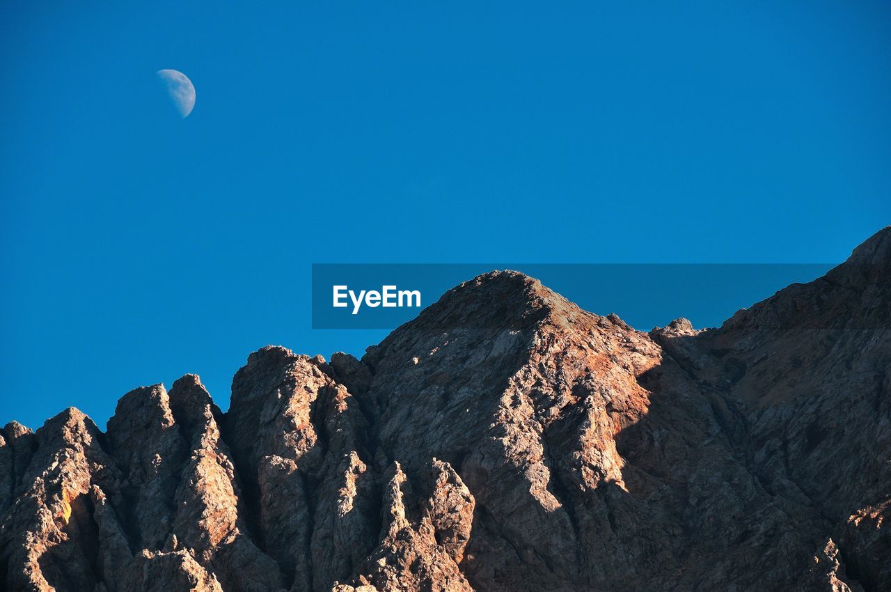 Low angle view of rocky mountains against clear blue sky