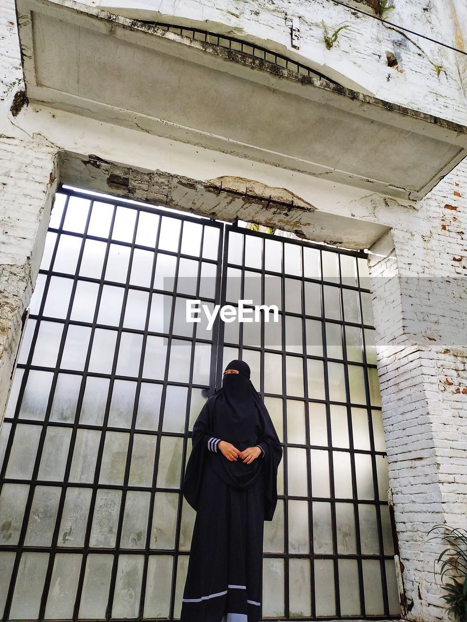 Woman wearing black hijab standing against gate