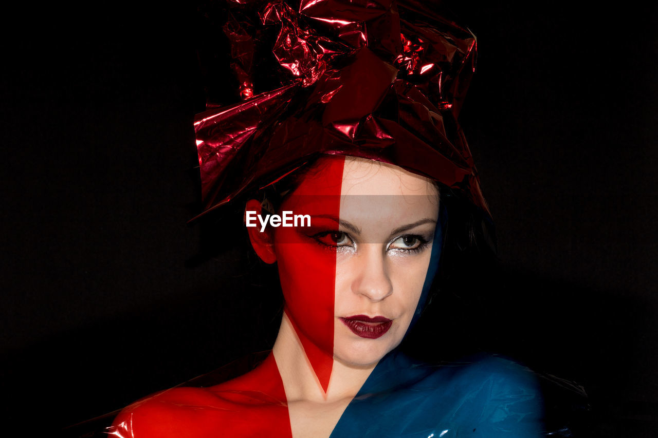 Close-up of thoughtful female model with plastic against black background