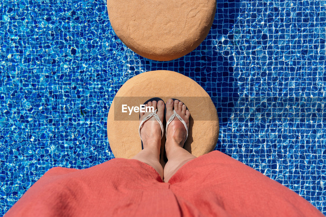 LOW SECTION OF WOMAN WEARING HIGH HEELS STANDING BY SWIMMING POOL