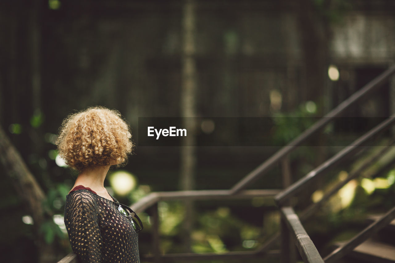 Side view of mid adult woman with curly hair standing by railing