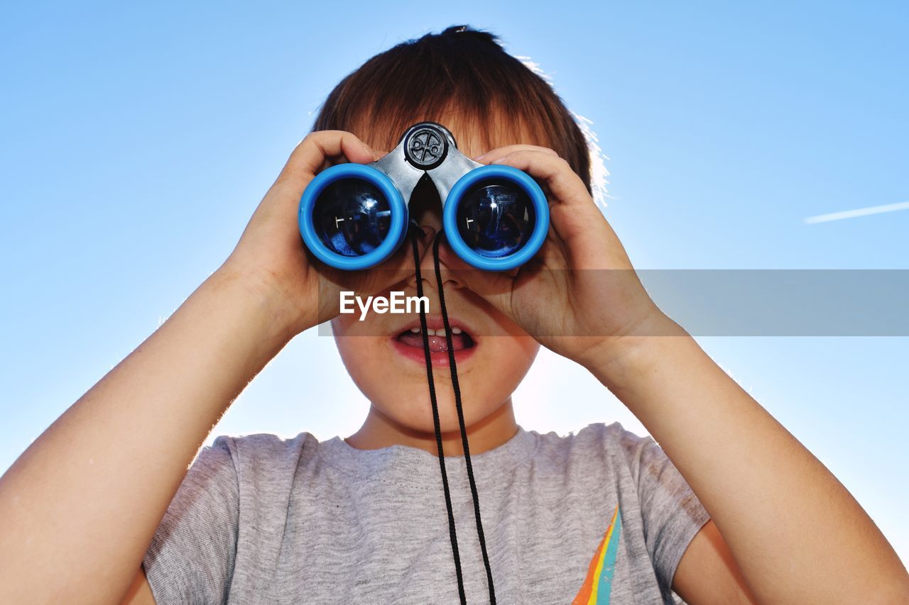 Boy looking through binocular against clear sky
