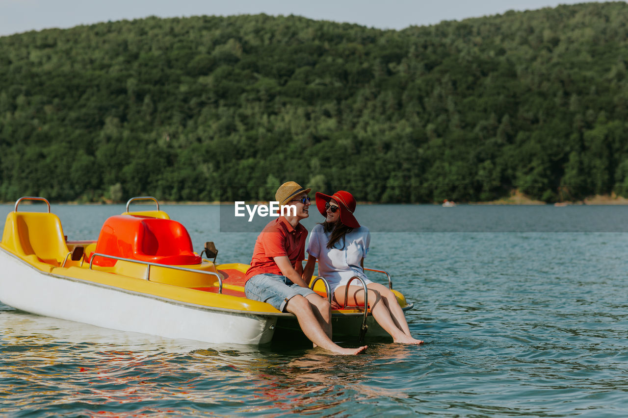 Cheerful man and woman in paddleboat on lake against sky