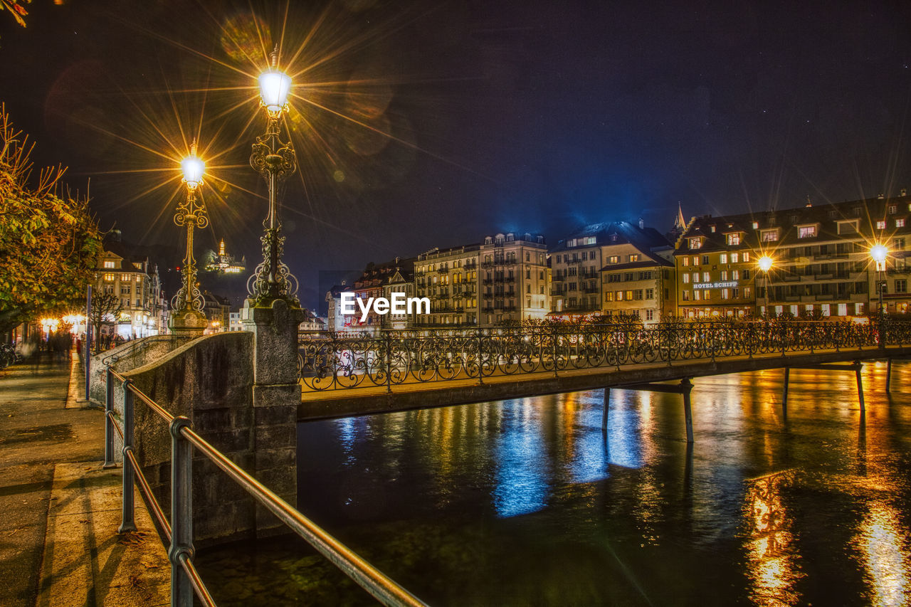 Illuminated city by river against sky at night