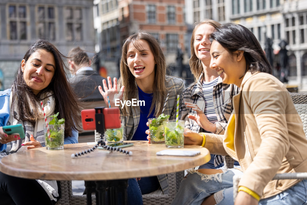 Smiling friends talking on video call while having food at restaurant