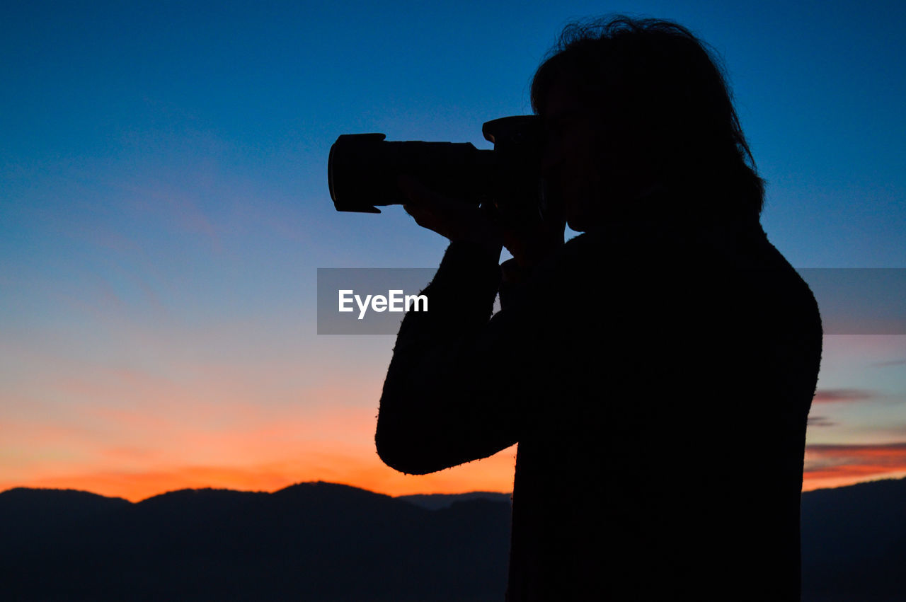 Silhouette man photographing against sky during sunset