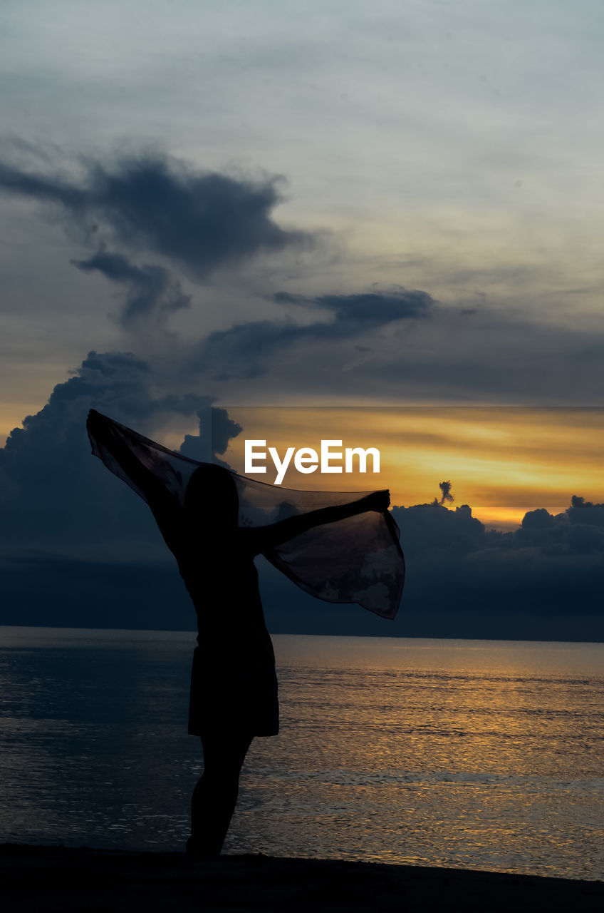 Silhouette girl standing on beach against sky during sunset