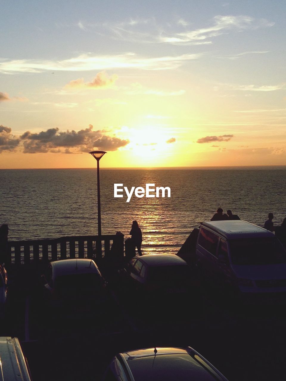 Calm sea at sunset with vehicles in foreground