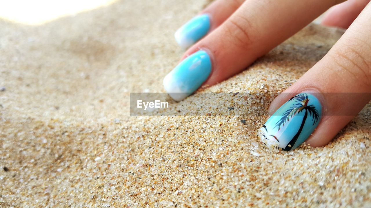 Cropped fingers of woman on sand at beach