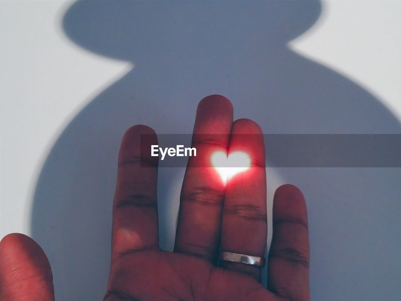 Close-up of human hand with beam of light shaping into a heart when projected in between fingers.