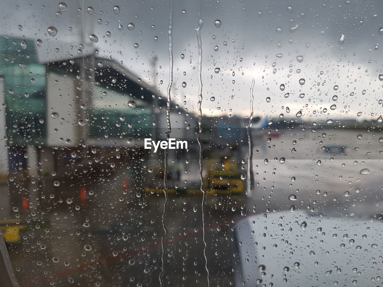 Buildings against cloudy sky seen through wet window