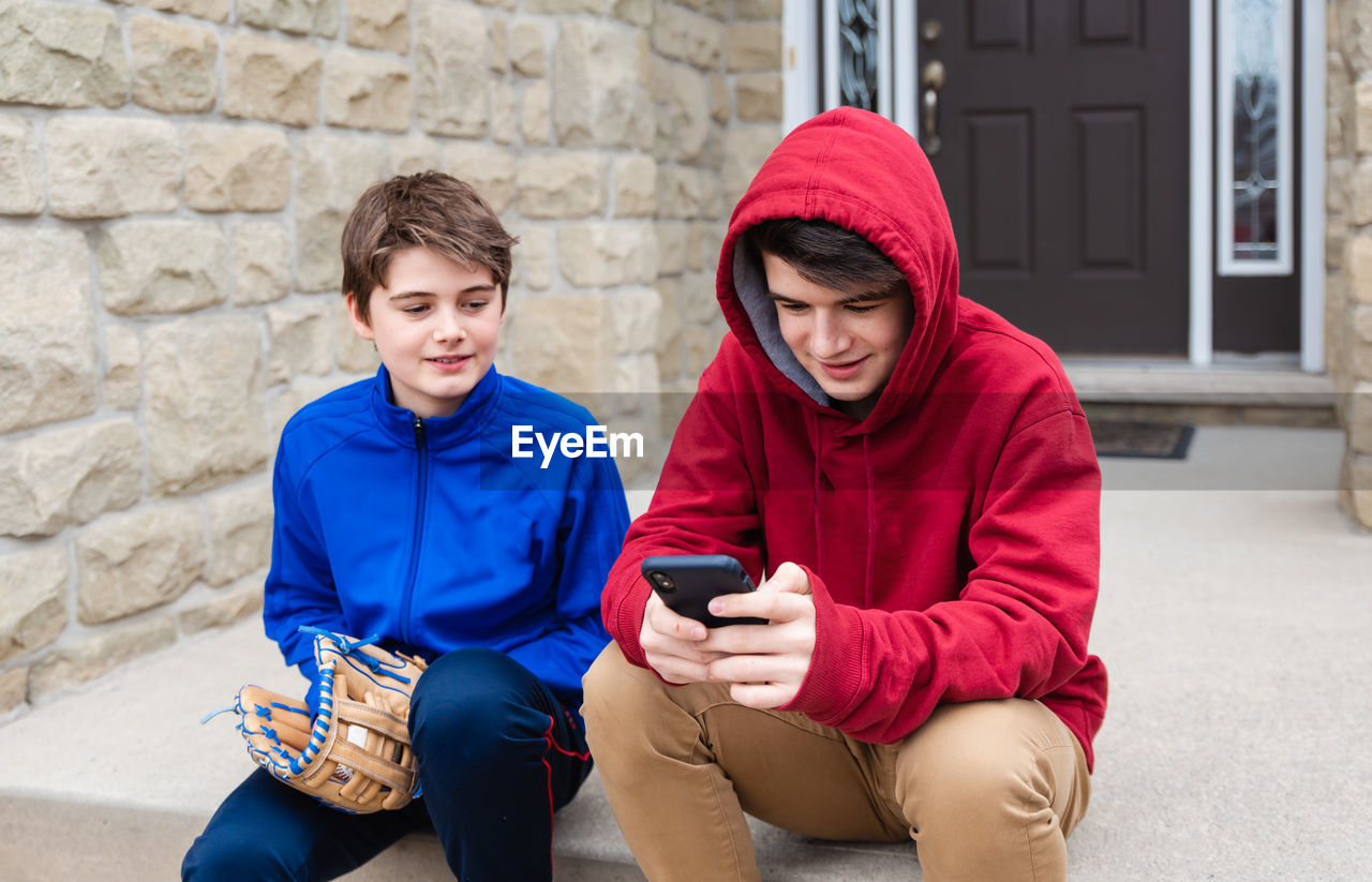 Two teenage boys sitting and talking on the front steps of a house.