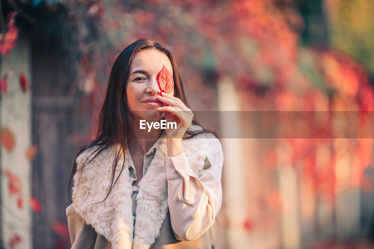 PORTRAIT OF BEAUTIFUL YOUNG WOMAN STANDING AGAINST BLURRED BACKGROUND