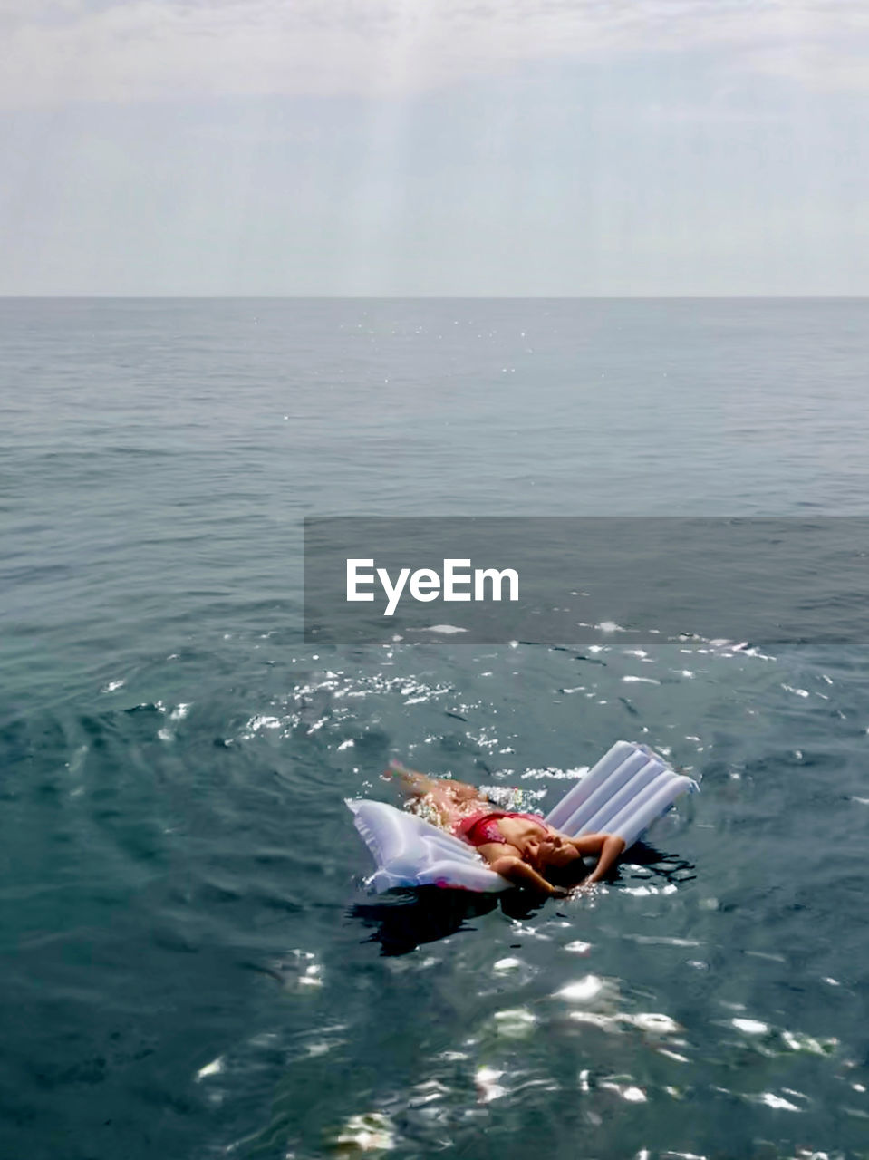 High angle view of woman lying over inflatable raft in sea against sky