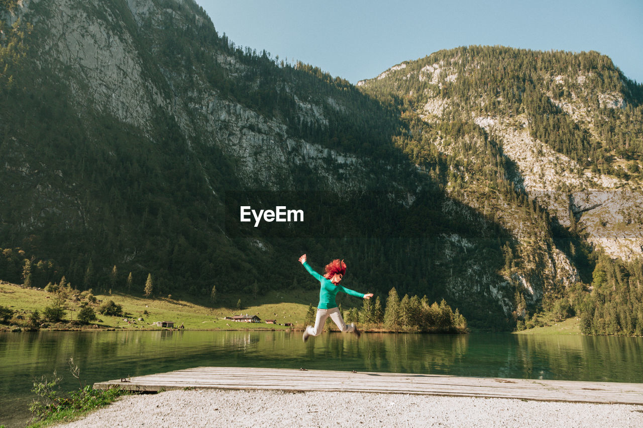 Happy woman jumping on pier against mountain