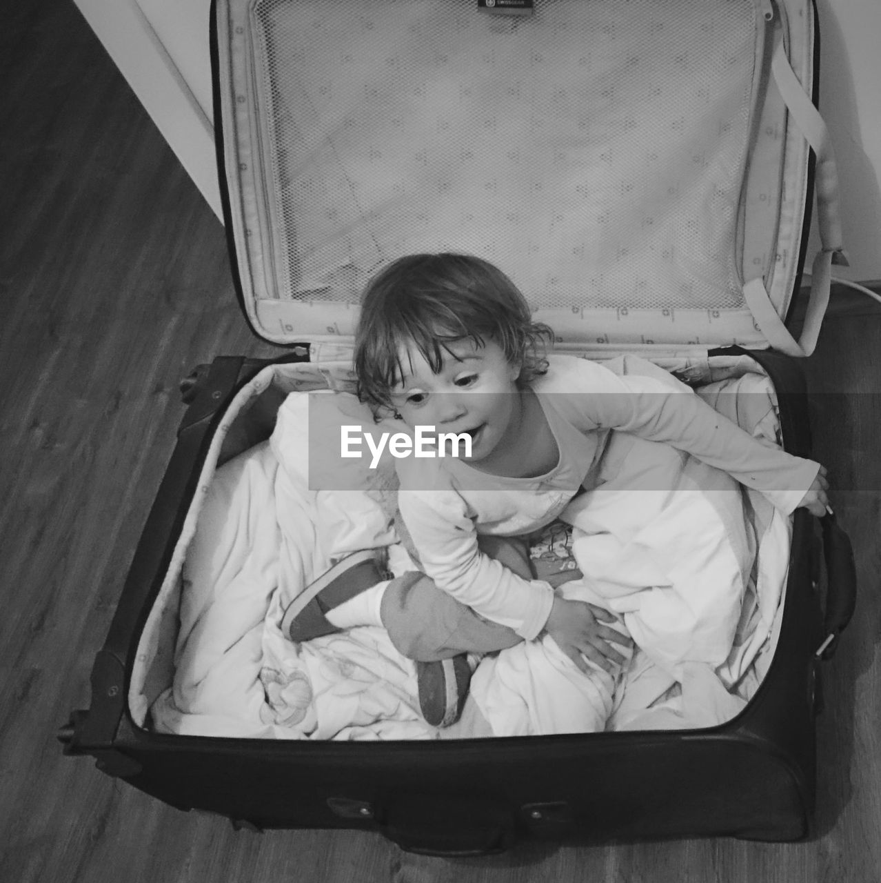 High angle view of playful girl sitting in suitcase