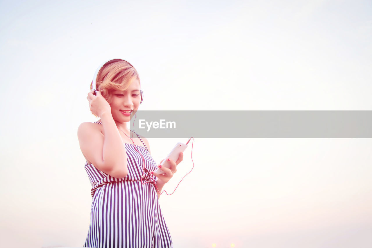 Low angle view of woman listening music against sky