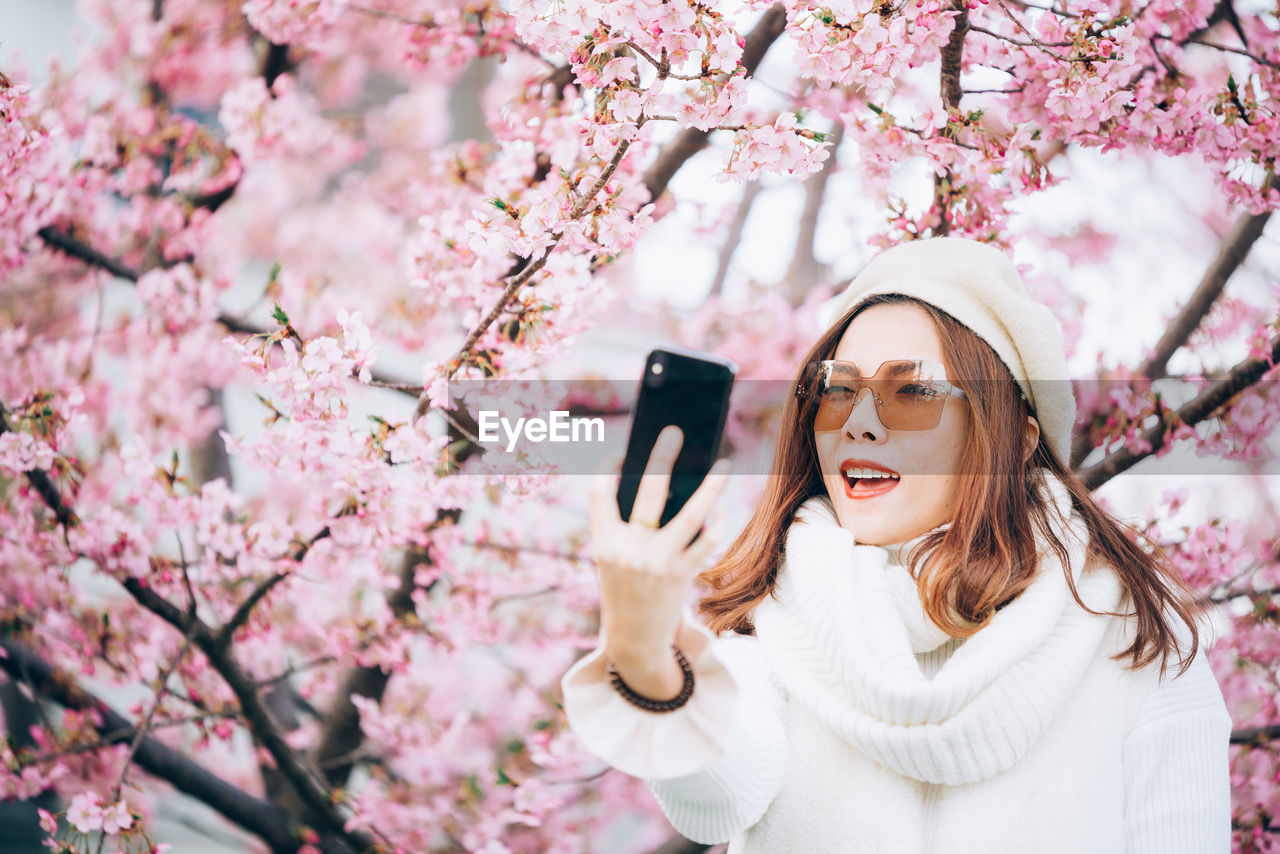 Beautiful woman taking selfie by cherry tree