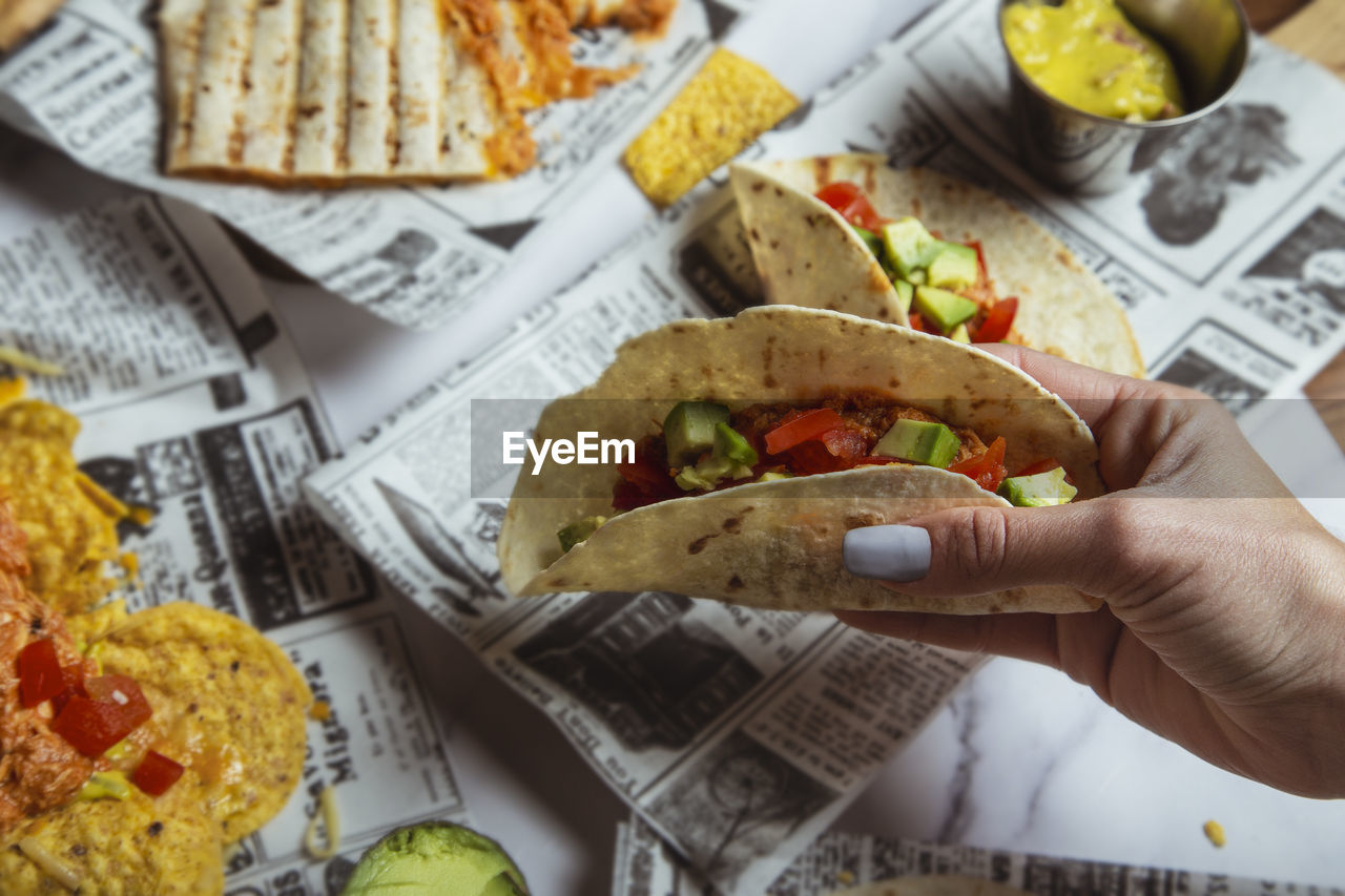 Female hands hold mexican beef tacos with vegetables on restaurant table. top view person