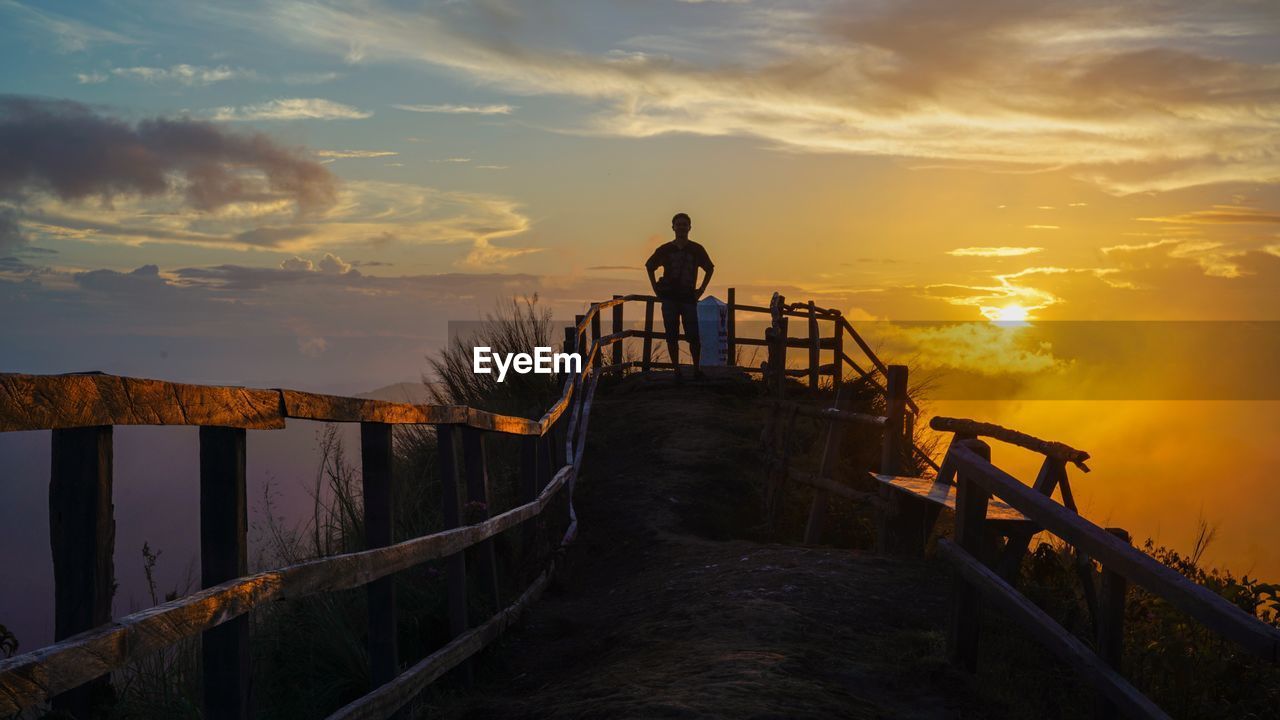 Silhouette man standing by railing against sky during sunset