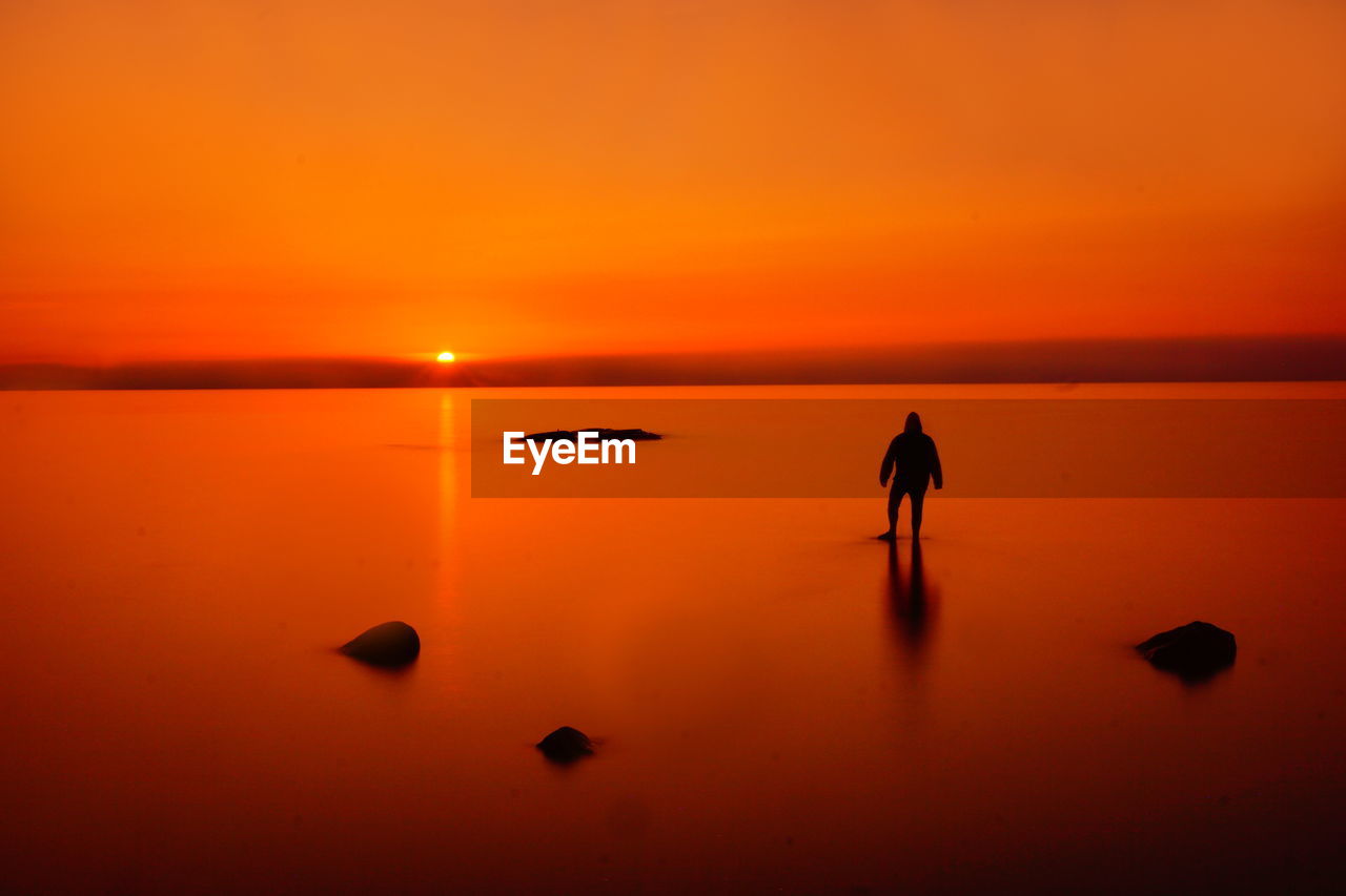 Silhouette woman standing at beach against sky during sunset