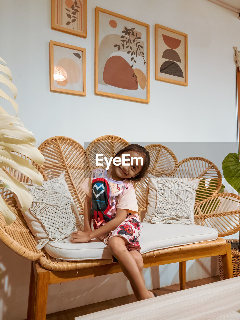 Happy little girl sitting on the rattan couch in a boho interior design.