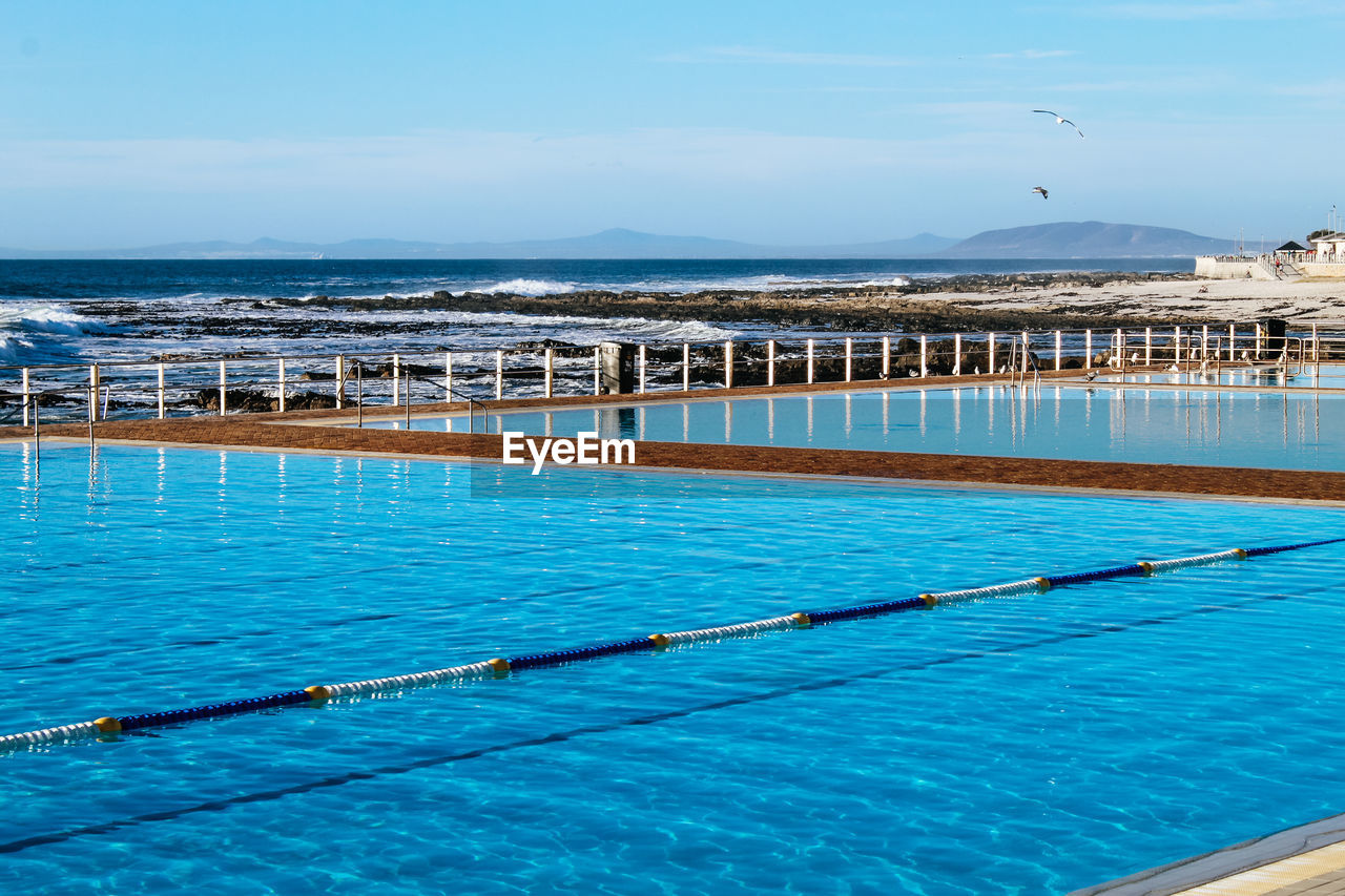 HIGH ANGLE VIEW OF SWIMMING POOL AGAINST SEA