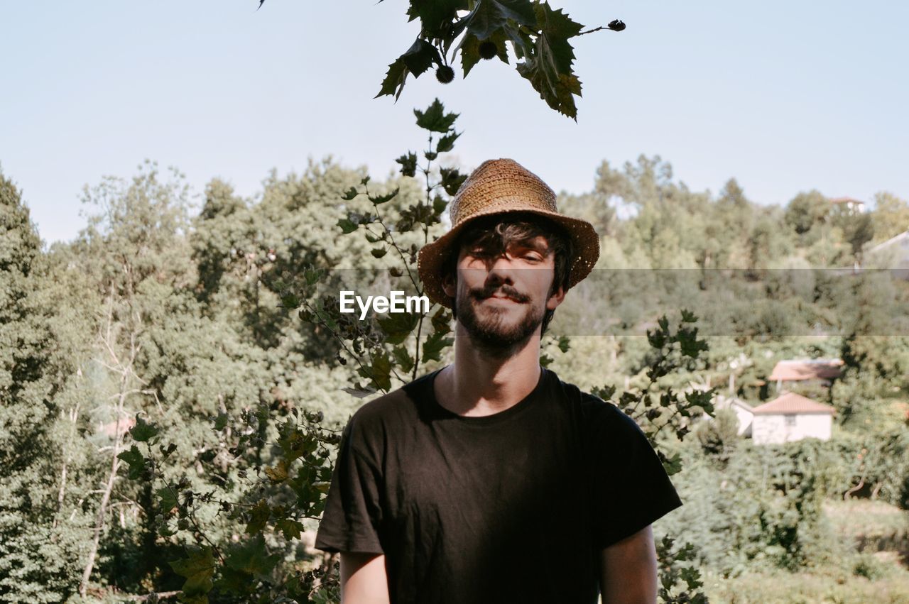 Portrait of young man standing against trees