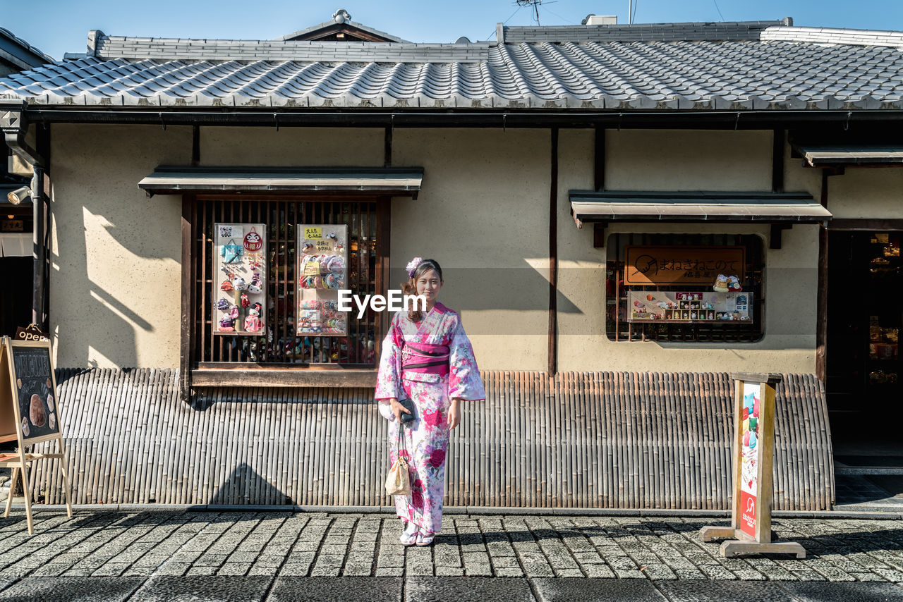 Woman wearing kimono while standing on street against building