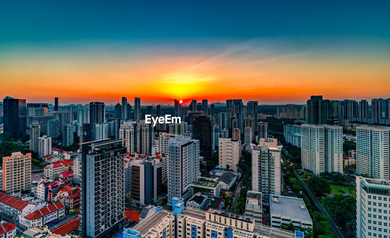 HIGH ANGLE VIEW OF MODERN CITY BUILDINGS AGAINST SKY DURING SUNSET