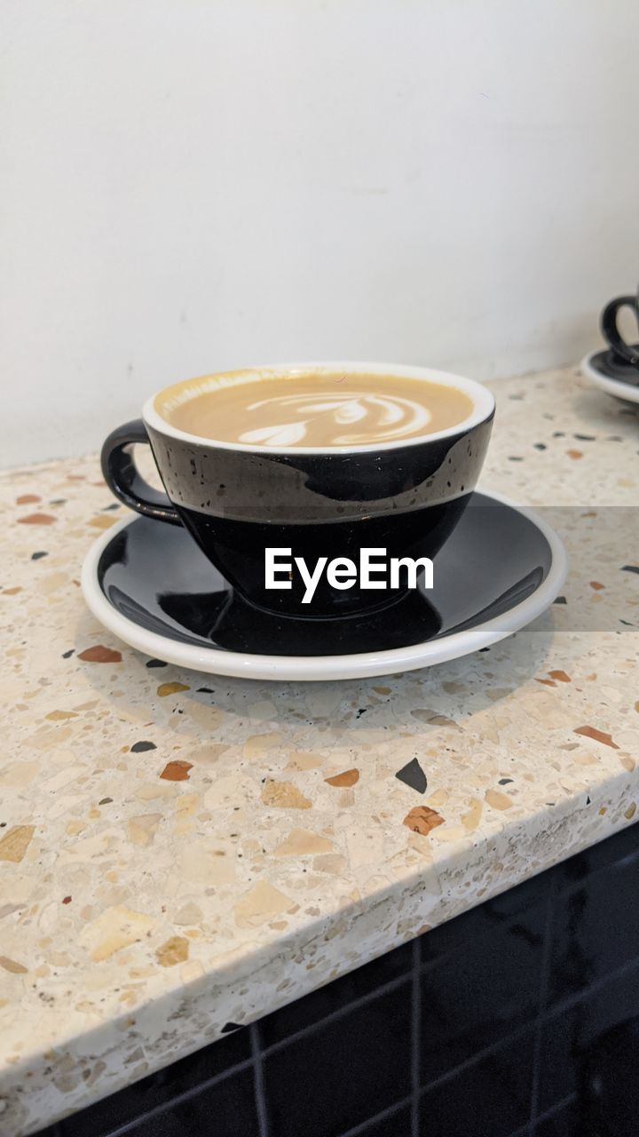 HIGH ANGLE VIEW OF COFFEE CUP ON TABLE AGAINST WALL