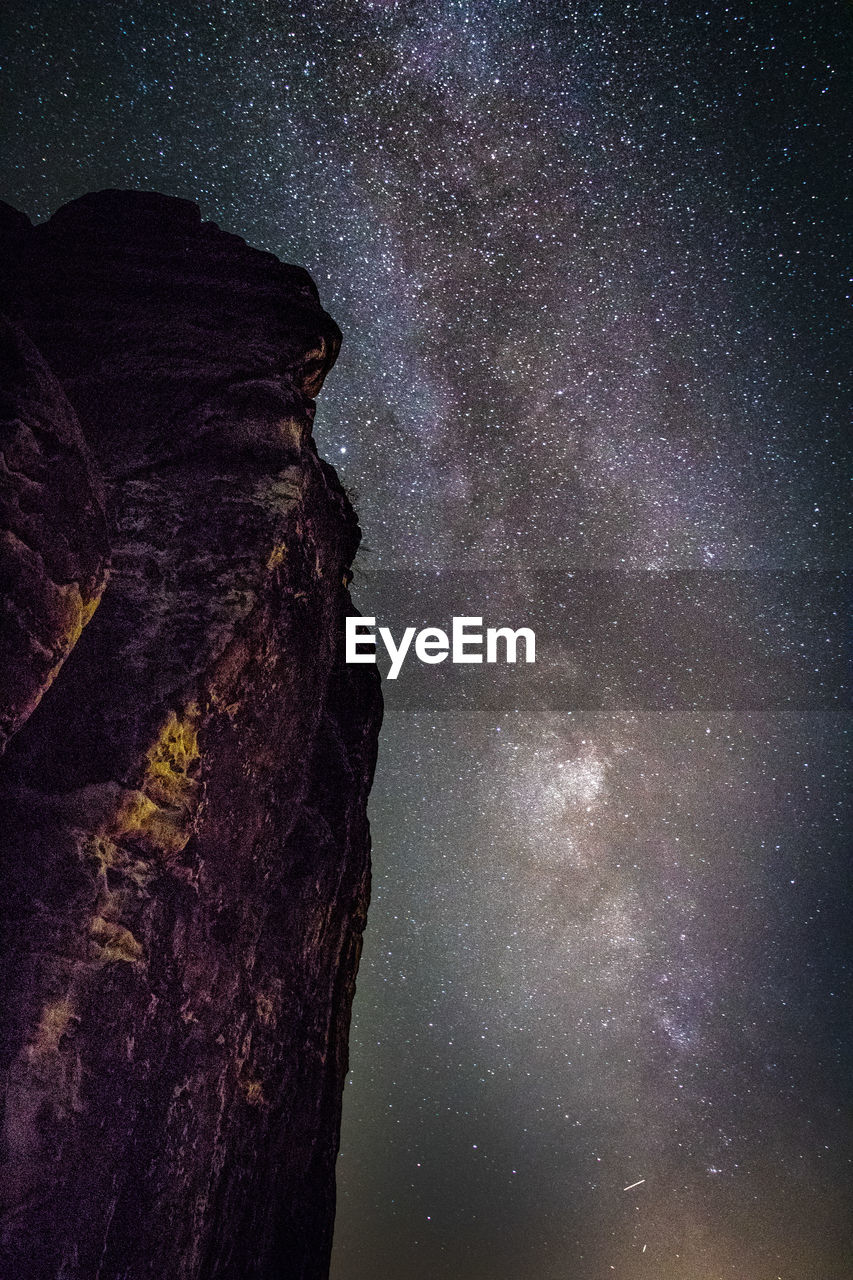 Low angle view of rocky mountain against star field at night