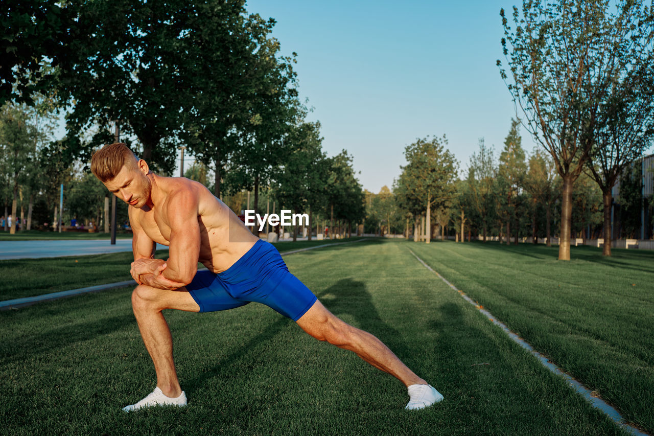 SIDE VIEW OF MAN WITH ARMS RAISED ON GRASS