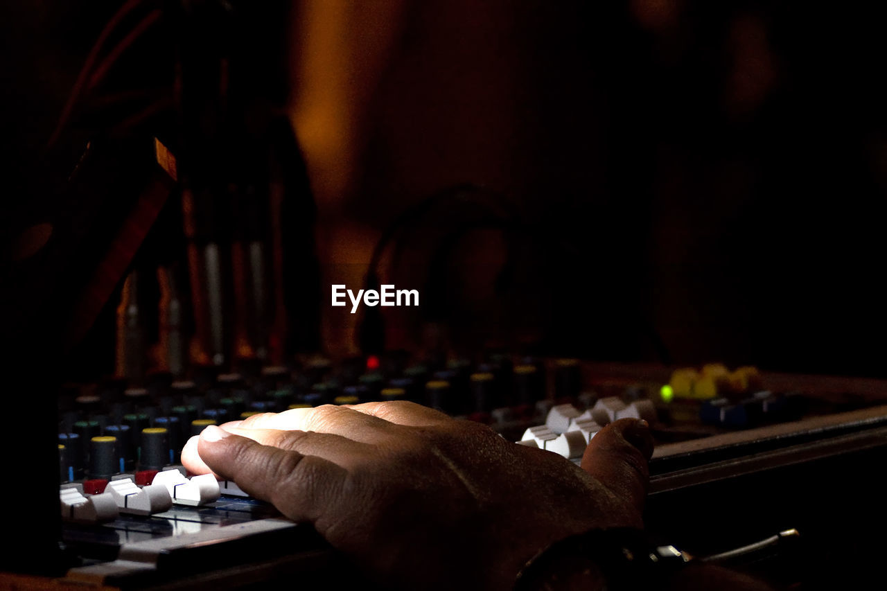 Cropped hand of dj using sound mixer in darkroom