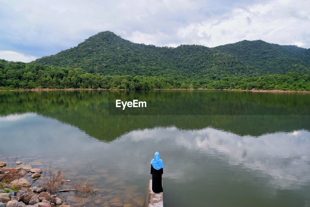 REAR VIEW OF MAN STANDING ON LAKE AGAINST SKY