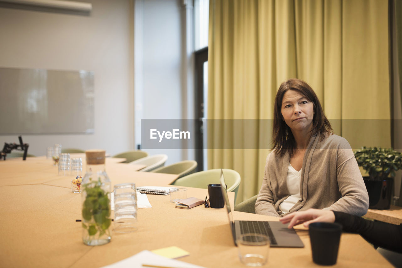 Serious businesswoman sitting with colleague at conference table in board room