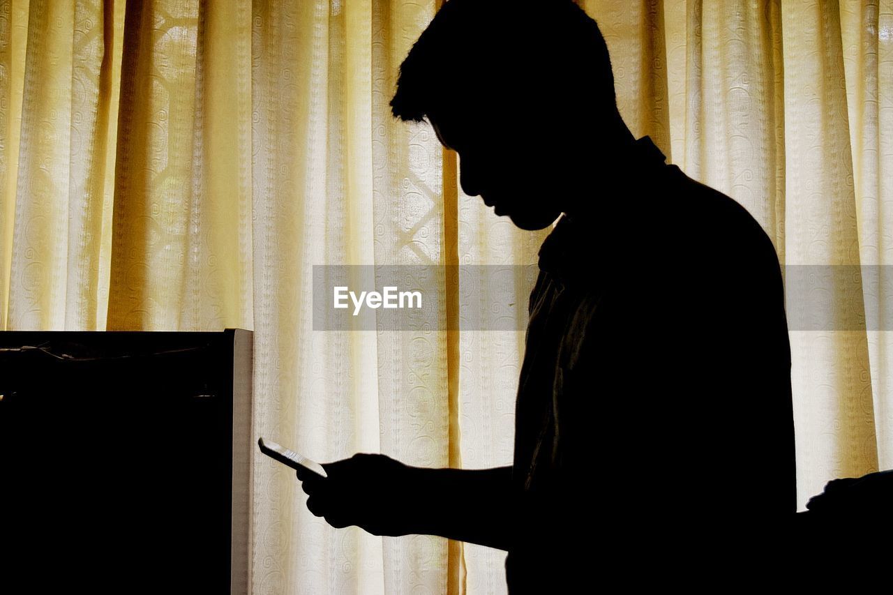 SIDE VIEW OF SILHOUETTE MAN HAND AGAINST CURTAIN