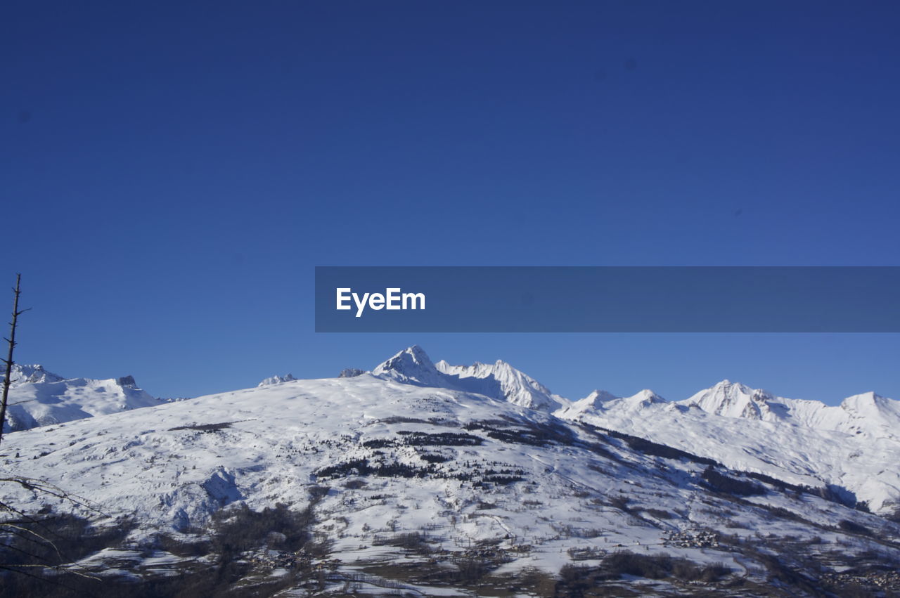 Low angle view of snowcapped mountains against clear blue sky