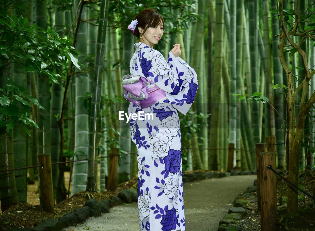 Woman standing by plants against trees 