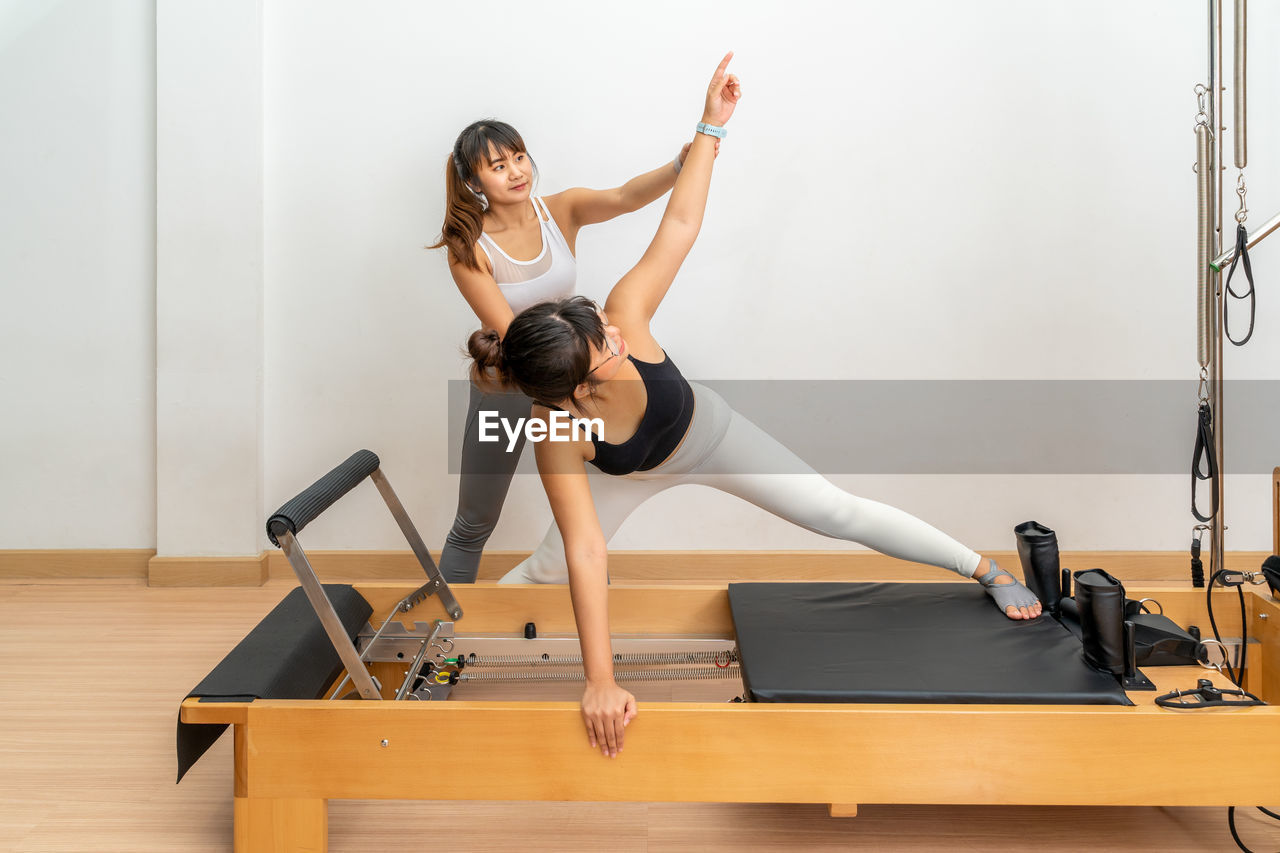 Young asian woman working on pilates reformer machine with a female trainer during exercise training