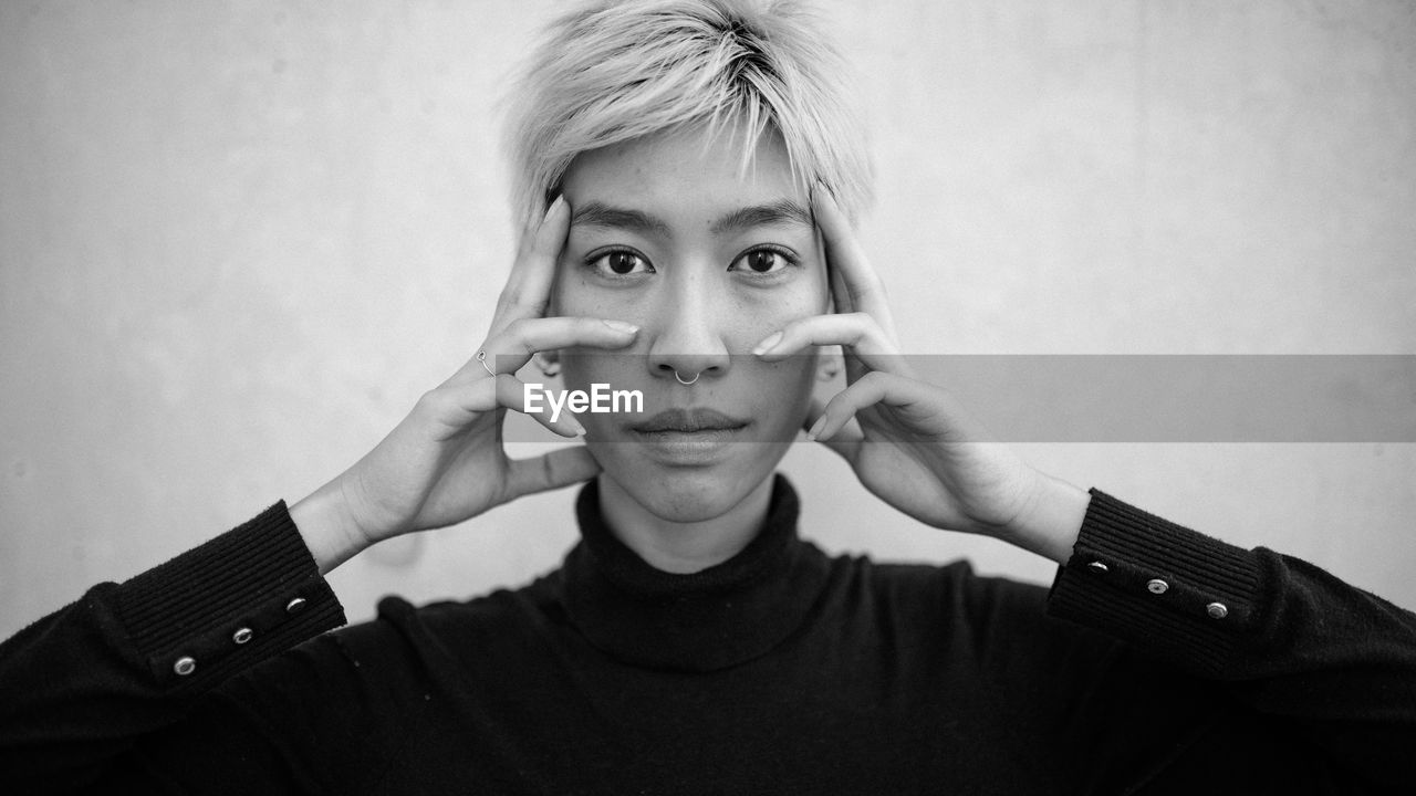 Portrait of woman touching cheek against wall