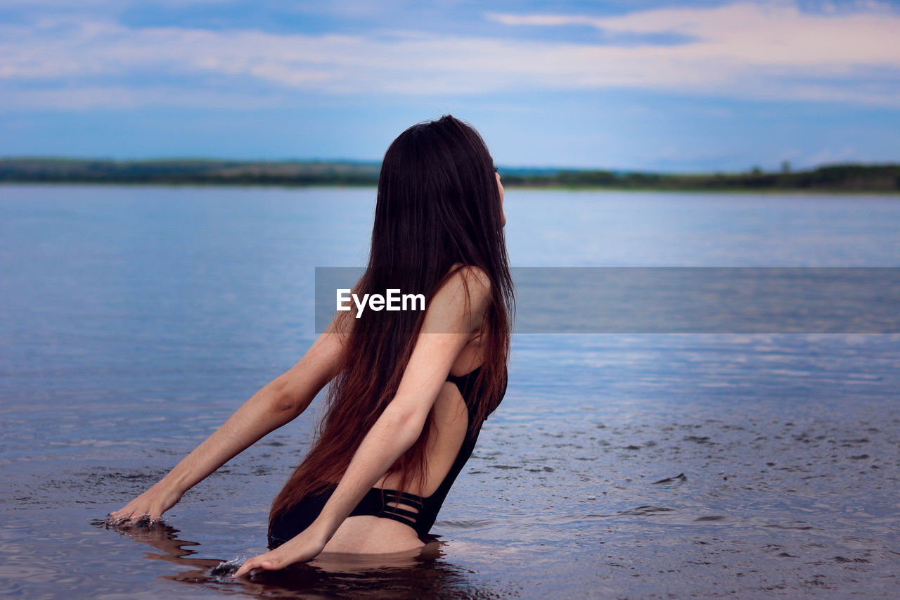 Sensuous young woman standing in sea against sky