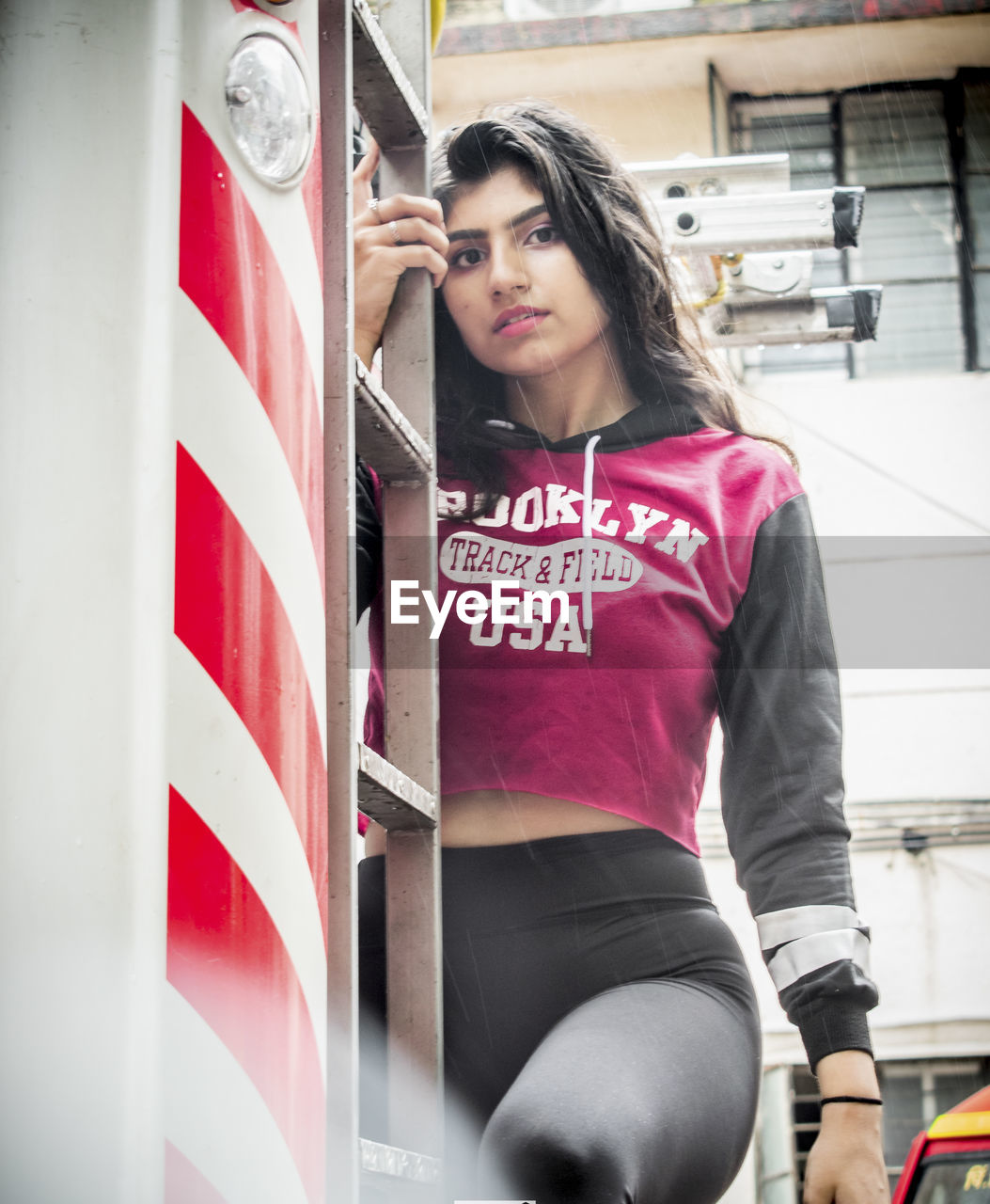 Portrait of young woman standing on fire engine aginst building