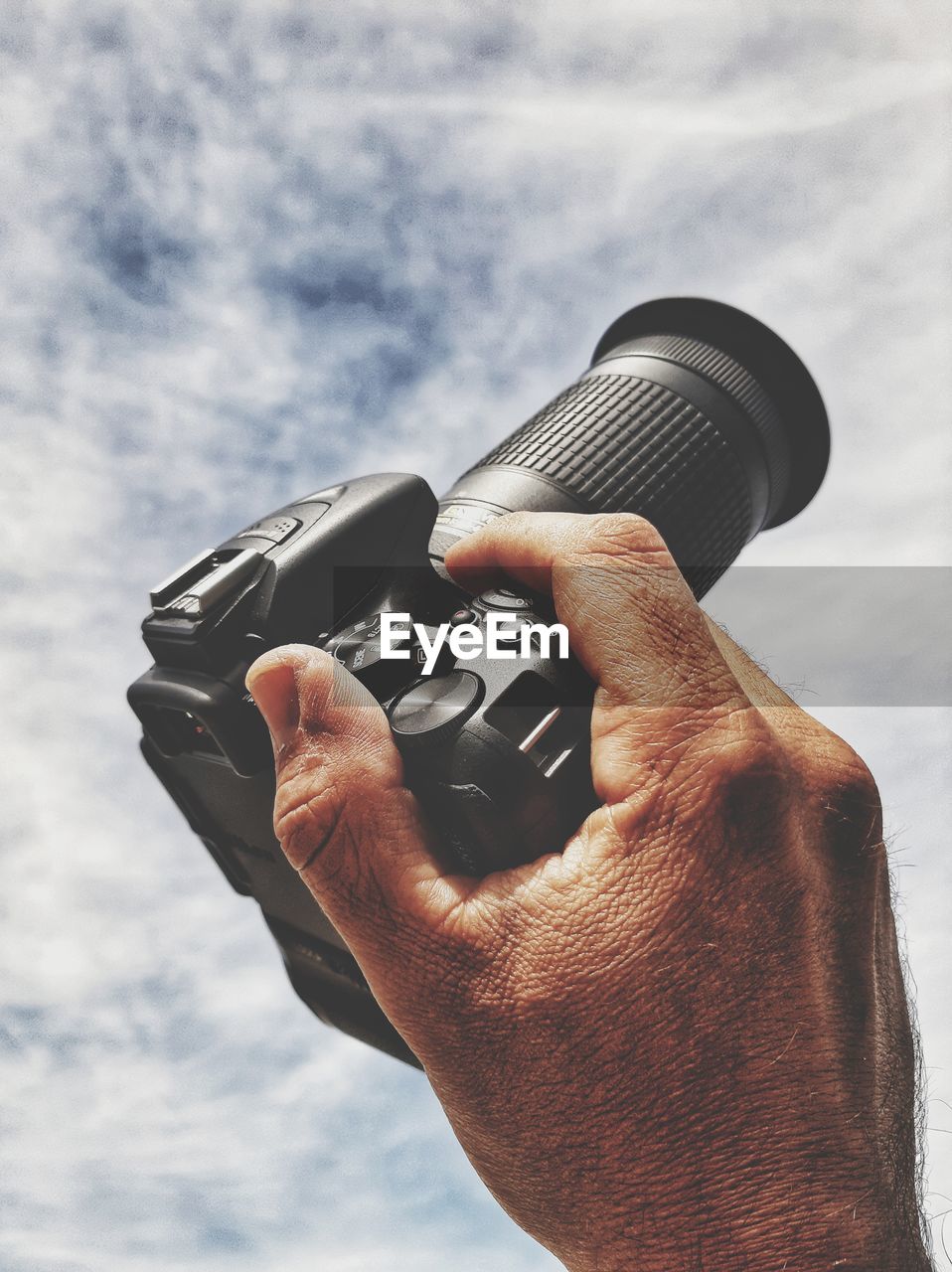 CLOSE-UP OF PERSON HOLDING CAMERA AGAINST SKY